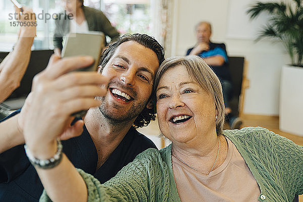 Lächelnde ältere Frau  die mit einem männlichen Mitarbeiter im Gesundheitswesen Selbsthilfe betreibt  während sie im Altenheim sitzt