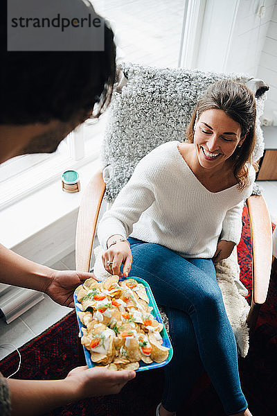 Lächelnde Frau nimmt während der Party zu Hause Snacks von Freundin ein