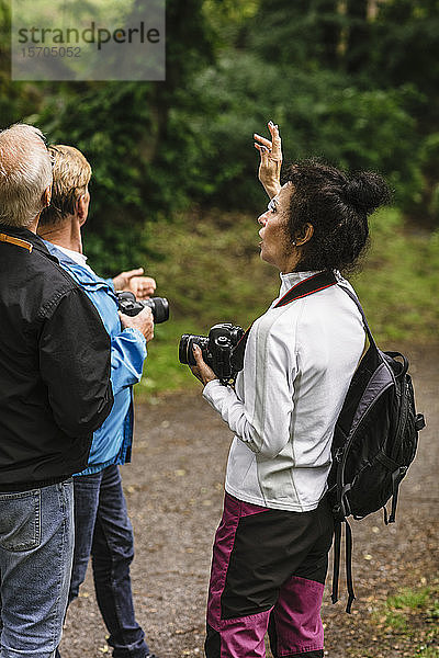 Weibliche Ausbilderin gestikuliert  während sie älteren Männern während eines Fotokurses Erklärungen gibt