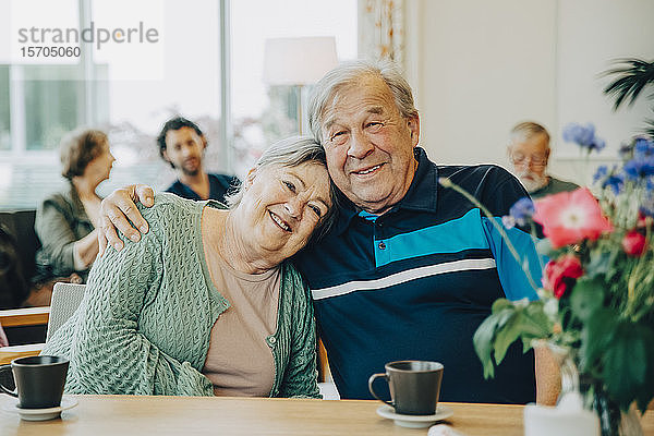 Porträt von älteren älteren Freunden  die mit dem Arm um den Esstisch im Pflegeheim sitzen