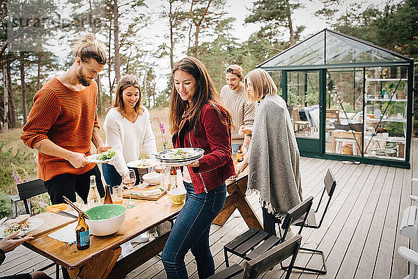 Männliche und weibliche Freunde  die nach dem Abendessen auf der Terrasse Tellerreste tragen