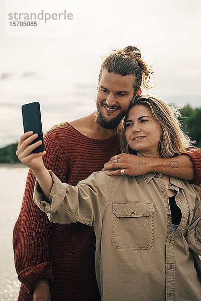 Lächelndes Paar  das sich am Handy gegen den Himmel bewegt