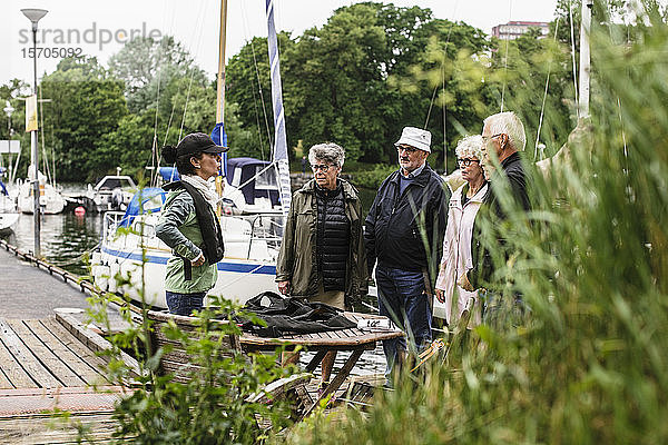 Weibliche Ausbilderin erklärt älteren Männern und Frauen  wie sie während des Bootsführerkurses auf dem Pier stehen