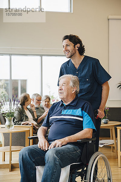 Lächelnder Krankenpfleger schiebt behinderten älteren Mann auf Rollstuhl im Altersheim