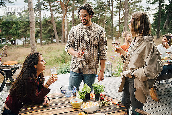 Lächelnde Freunde genießen Getränke während eines Gesprächs während einer Gartenparty im Hof