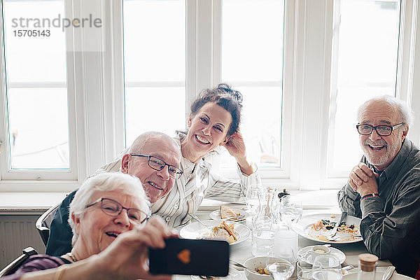 Frau klickt Foto von älteren Freunden über Smartphone an  während sie im Restaurant sitzt