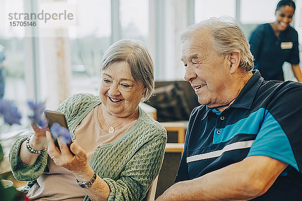 Lächelnde ältere Frau teilt Smartphone mit Mann  während sie im Altersheim sitzt