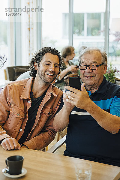 Älterer Mann  der sich mit seinem Enkel am Esstisch in einem Altenpflegeheim vergnügt