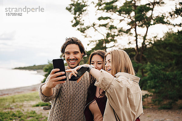 Fröhliche Freunde  die sich am Strand am Smartphone vergnügen