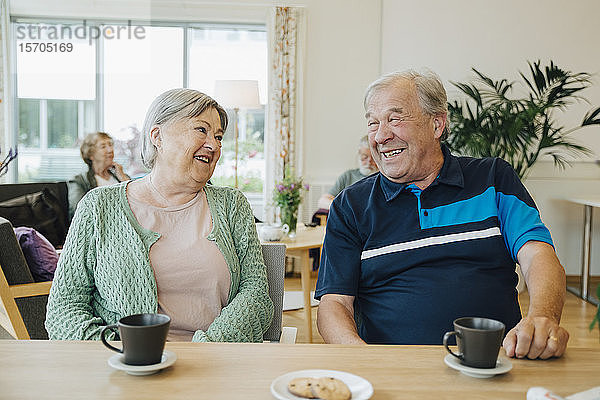 Lächelnde ältere Senioren  die sich unterhalten  während sie am Esstisch im Pflegeheim sitzen