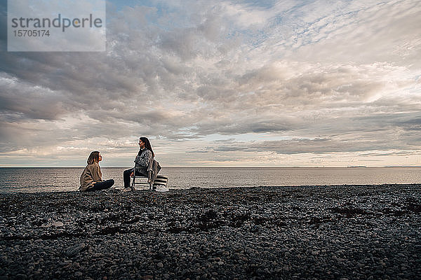 Freunde unterhalten sich  während sie sich am Meeresufer am Strand vor bewölktem Himmel ausruhen