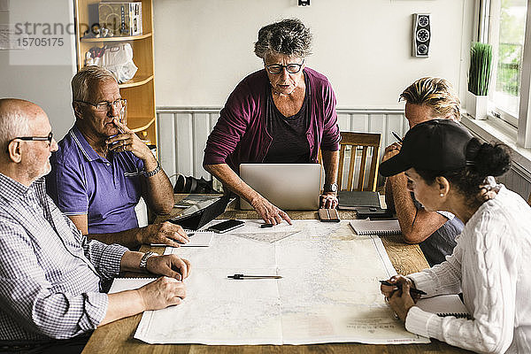 Weibliche Ausbilderin erklärt älteren Männern und Frauen während des Navigationskurses über Karte am Tisch