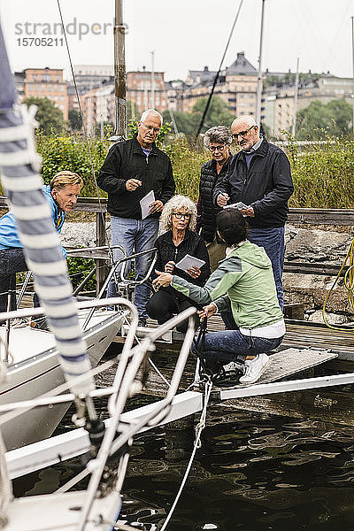 Ältere Männer und Frauen hören während des Bootsführerkurses dem weiblichen Ausbilder auf der Yacht zu