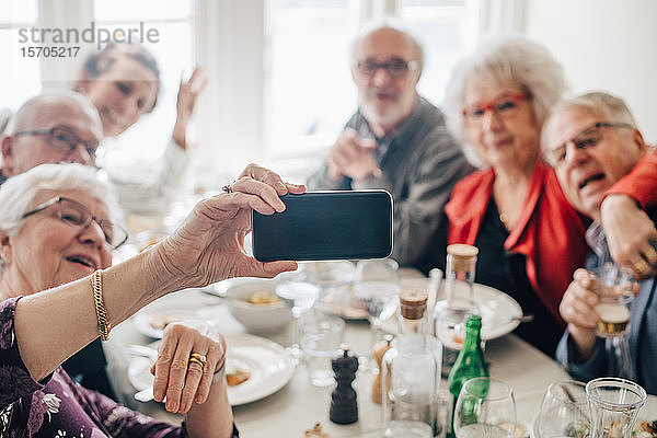 Frau klickt Foto von älteren Freunden über Smartphone an  während sie im Restaurant sitzt