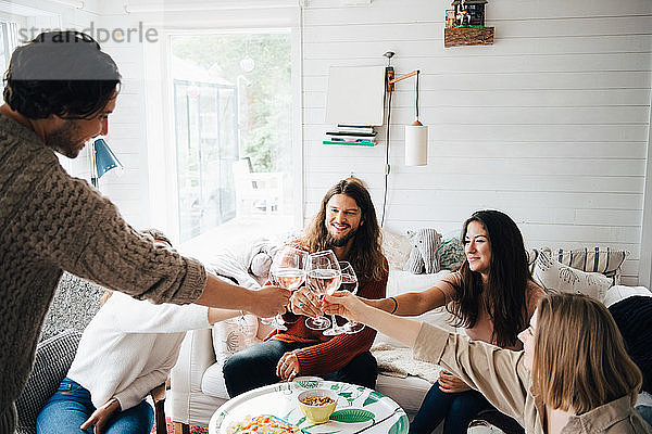 Männliche und weibliche Freunde stoßen bei Tisch in einer Hütte mit Weingläsern auf das Essen an