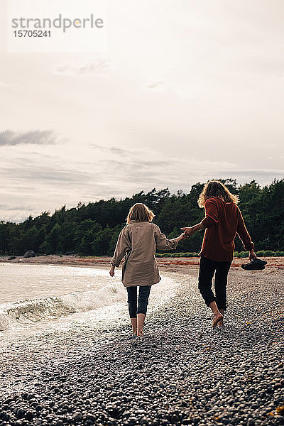 Rückansicht eines Paares beim gemeinsamen Spaziergang am Meeresufer am Strand gegen den Himmel