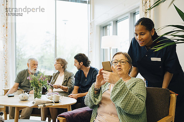 Pensionierte ältere Frau teilt Smartphone mit junger Krankenschwester bei Gemeindeeinsätzen
