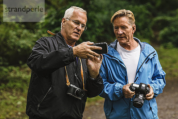 Älterer Mann zeigt einem Freund sein Handy während eines Fotokurses