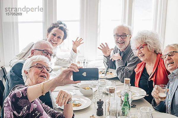 Frau klickt Foto von älteren Freunden per Smartphone an  während sie im Restaurant sitzt