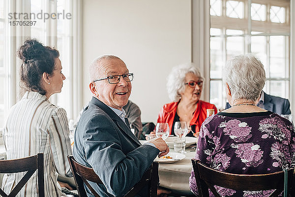 Porträt eines älteren Mannes  der lächelnd neben Freunden im Restaurant sitzt