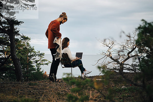 Mann hält Decke  während Frau mit Laptop im Wald gegen Himmel