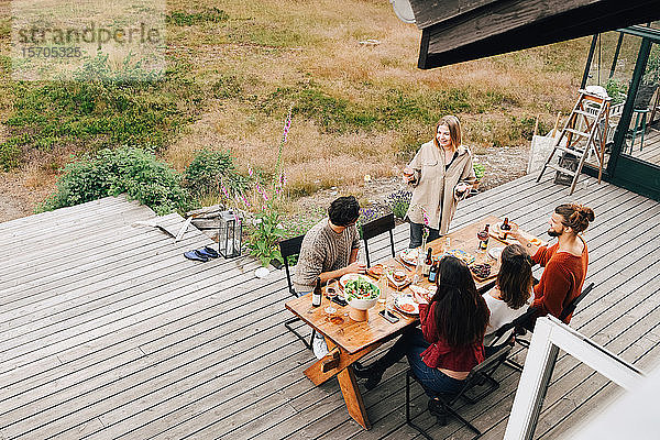 Schrägansicht einer Frau  die sich mit Freunden unterhält  während sie auf der Terrasse zu Abend isst