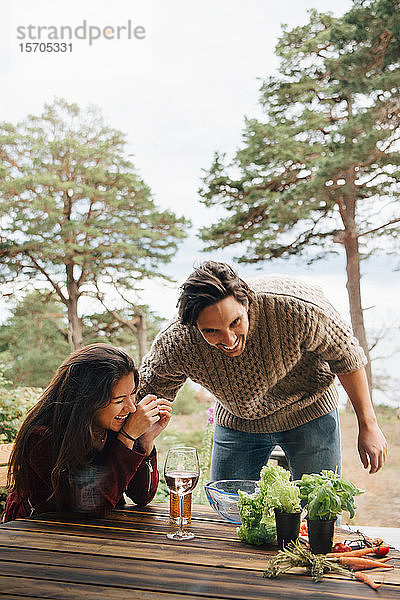 Mann und Frau im mittleren Erwachsenenalter haben Spaß bei der Zubereitung von Mahlzeiten am Tisch im Innenhof