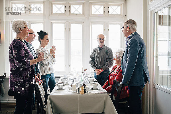 Ältere Frau sitzt am Restauranttisch  während männliche und weibliche Freunde am Tisch stehen