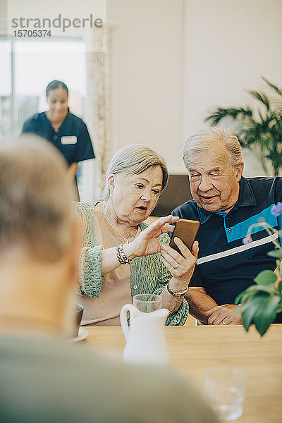 Ältere Frau teilt ein Smartphone mit einem Mann  während sie am Esstisch im Altenheim sitzt