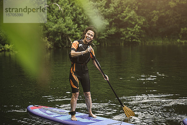 Porträt einer lächelnden älteren Frau beim Paddeln auf See während eines SUP-Kurses