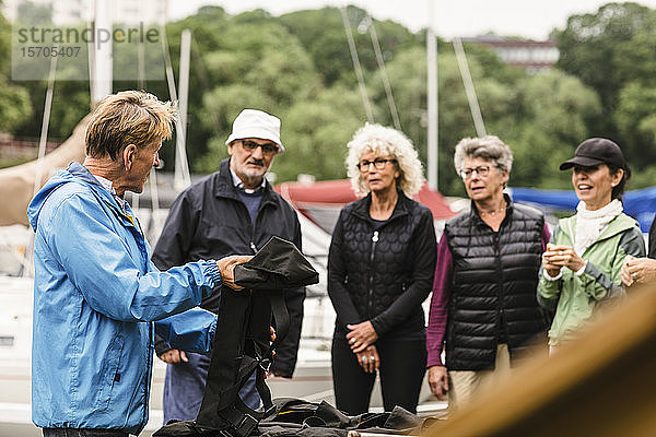 Männlicher Ausbilder erklärt älteren Männern und Frauen während des Bootsführerkurses die Schwimmweste