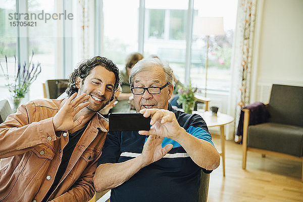 Videokonferenz zwischen einem älteren Mann und seinem Enkel mit einem Smartphone im Altenpflegeheim