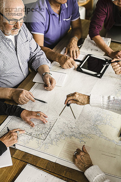 Hochwinkelansicht von älteren Männern und Frauen mit Karte am Tisch während des Navigationskurses