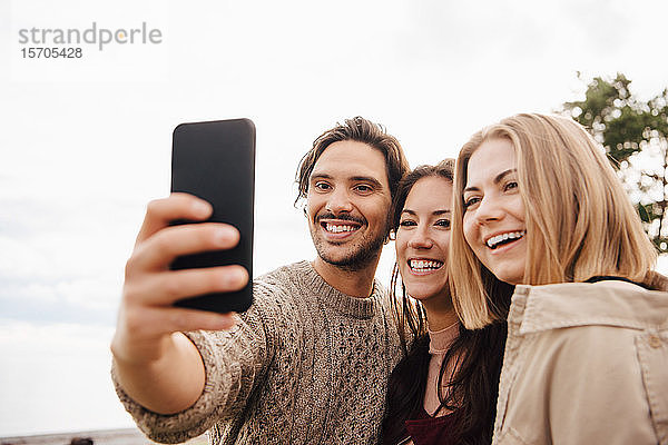Lächelnder Mann nimmt Selfie mit Freunden auf Smartphone gegen den Himmel