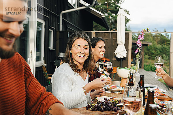 Lächelnde Frau schaut einen Freund an  während sie beim Abendessen in einer Party genießt