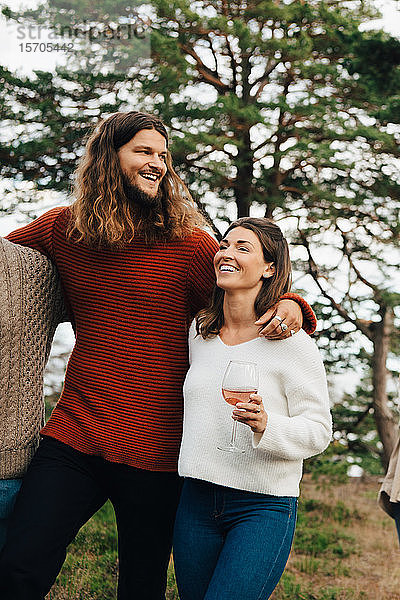 Glückliche Frau trinkt Wein  während sie mit einem lächelnden Freund im Freien spazieren geht