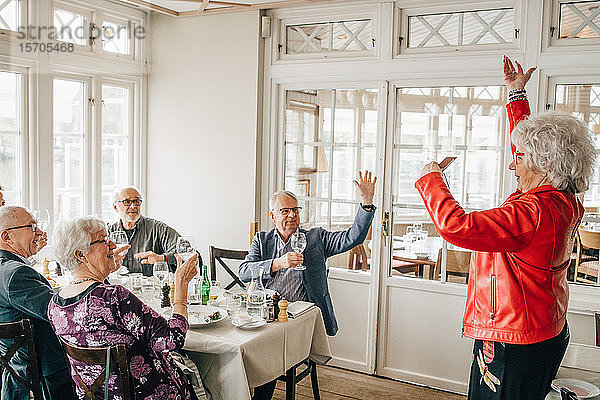 Ältere Frau gestikuliert  während männliche und weibliche Freunde im Restaurant sitzen