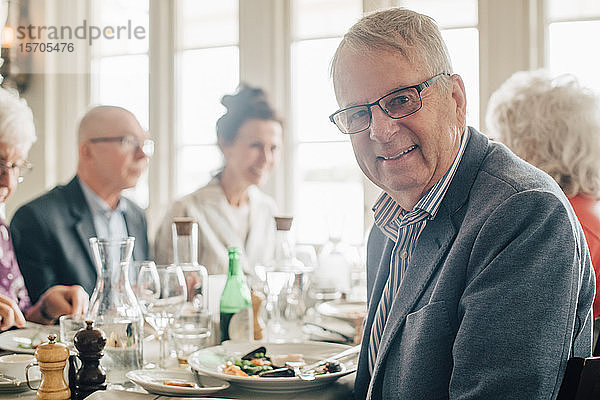 Porträt eines älteren Mannes  der lächelnd neben Freunden im Restaurant sitzt