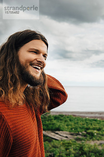 Nahaufnahme eines lächelnden Mannes mit langen Haaren am Strand