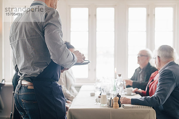 Mittelteil des Eigentümers  der am Tisch steht  während Mann und Frau im Restaurant sitzen