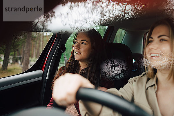 Lächelnde Freundinnen  die während der Fahrt im Auto wegschauen