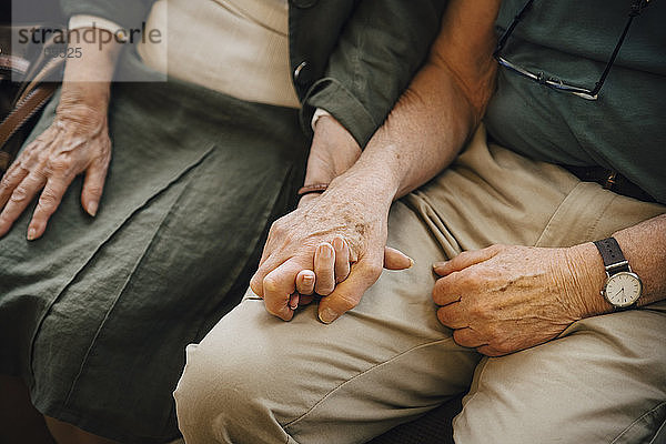 Mittelteil eines älteren Paares  das im Pflegeheim sitzend Händchen hält