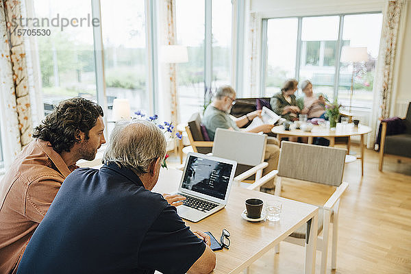 Mann hilft älterem Großvater mit Laptop am Esstisch im Altenheim