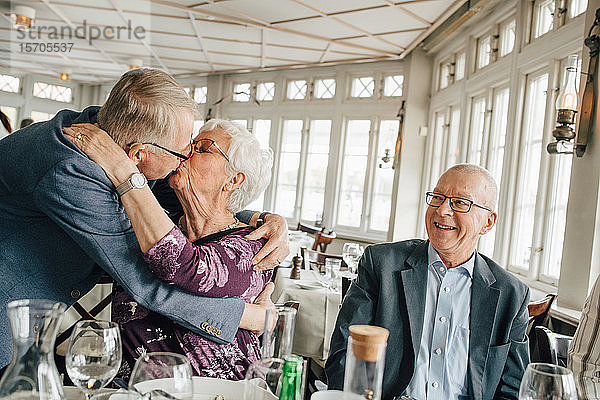Älteres Paar küsst sich  während ein männlicher Freund im Restaurant lächelt