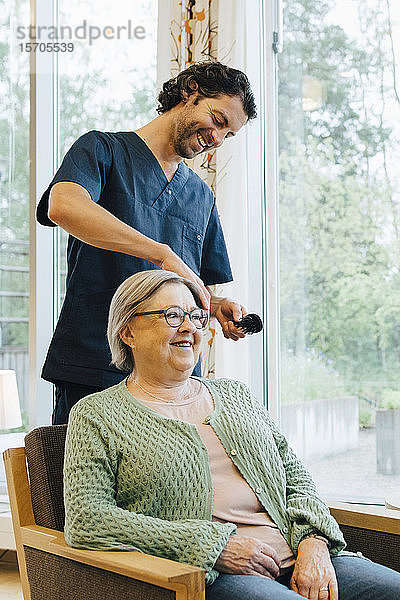 Lächelnder Pfleger bürstet älteren Frauen im Altersheim die Haare