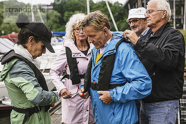 Älterer Mann hilft Freund beim Tragen der Schwimmweste während des Bootsführerkurses