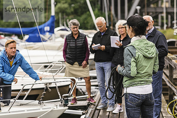 Weibliche Ausbilderin hält Seil  während sie älteren Männern und Frauen während des Bootsführerkurses Erklärungen gibt