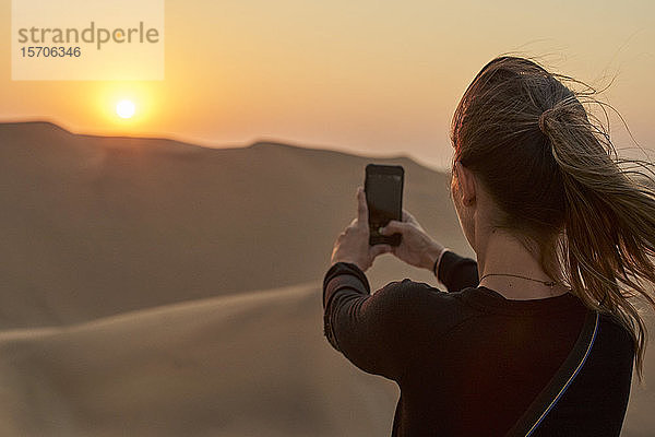 Frau macht ein Smartphone-Foto in der Wüste bei Sonnenuntergang  Düne 7  Walvis Bay  Namibia