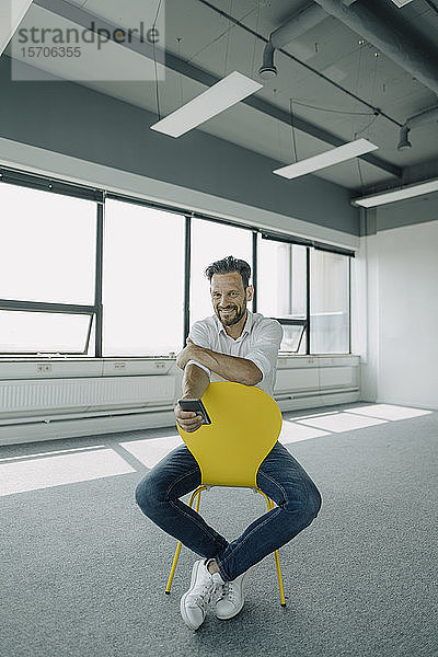 Porträt eines selbstbewussten reifen Geschäftsmannes auf gelbem Stuhl in einem leeren Büro