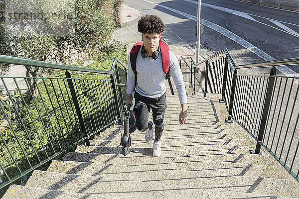 Junger Mann trägt E-Scooter auf Treppe